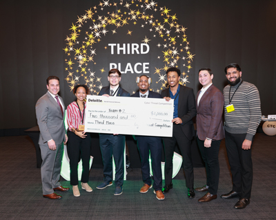 Daniel Lichowid Jr (third from left) and teammates hold up a cardboard check for $500 and stand in front of a wall reading 3rd place.